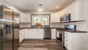 Une cuisine moderne avec des armoires blanches, des appareils en acier inoxydable et un parquet en bois disposé en chevrons.