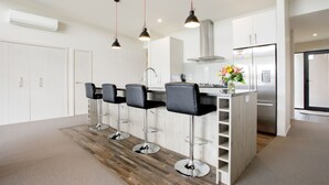 A modern kitchen with a central island, bar stools, pendant lighting, and a stainless steel refrigerator. - Daniels Delight (Wānaka)