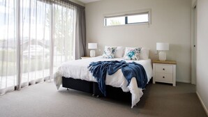 A bedroom with a bed, two bedside tables, a window with curtains, and a view of the outside. - Daniels Delight (Wānaka)