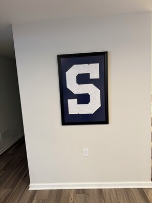 A framed letter 'S' on a plain wall in a room with wooden flooring.