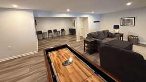 Moderni olohuone, jossa on shuffleboard-pöytä, harmaa sohva ja ruokailutila tuoleineen.