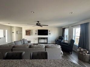 A living room with a sectional sofa, a flat-screen TV, a ceiling fan, and a window with curtains. - Cozy Home minutes to State College, Penn State & Historic Bellefonte. Sleeps 14 (Pleasant Gap)