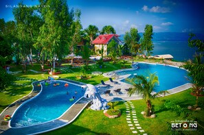 Un resort con un amplio espacio de piscina, un edificio de techo rojo y vista al mar.