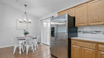 Une cuisine moderne avec des meubles en bois, un réfrigérateur en acier inoxydable et un coin repas avec des chaises et une table blanches.