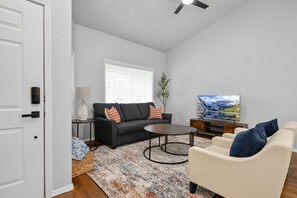 Una sala de estar con sofá, sillón, mesa de centro y televisor.