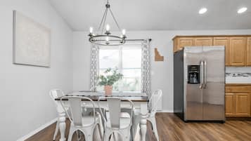 Une cuisine moderne avec des meubles en bois, un réfrigérateur en acier inoxydable et un coin repas comprenant une table en bois et des chaises blanches.