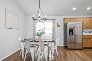Una cocina moderna con armarios de madera, un refrigerador de acero inoxidable y un comedor con mesa de madera y sillas blancas.