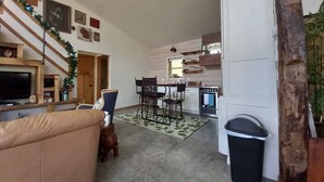 A cozy living room with a sofa, a TV, and a staircase leading to another room. - Mee Mee's Cabin Retreat- River, nature, small town, Hot Tub
 (Genoa)