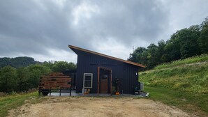 A rustic cabin with a sloped roof, a wooden door, and a small porch area with potted plants and pumpkins. - Mee Mee's Cabin Retreat- River, nature, small town, Hot Tub
 (Genoa)