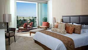 Habitación de hotel con una cama grande, un balcón con sillas y vistas al exterior.
