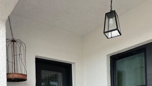 A black door with a glass panel, a hanging birdcage, a stone-tiled porch, and a window with a white frame.