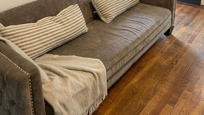 A living room with a sofa, two striped pillows, a blanket, and a painting on the wall.