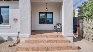 A house with a white exterior, a front door, a window, and a patio area with steps.