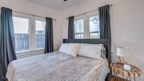A bedroom with a bed, curtains, a ceiling fan, and a bedside table with a lamp.