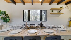 Un comedor con una mesa de madera dispuesta para seis personas, rodeada de sillas, y un ventanal grande arriba.