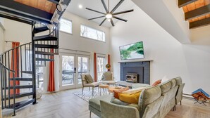 Un amplio salón con escalera, chimenea y un ventanal grande.