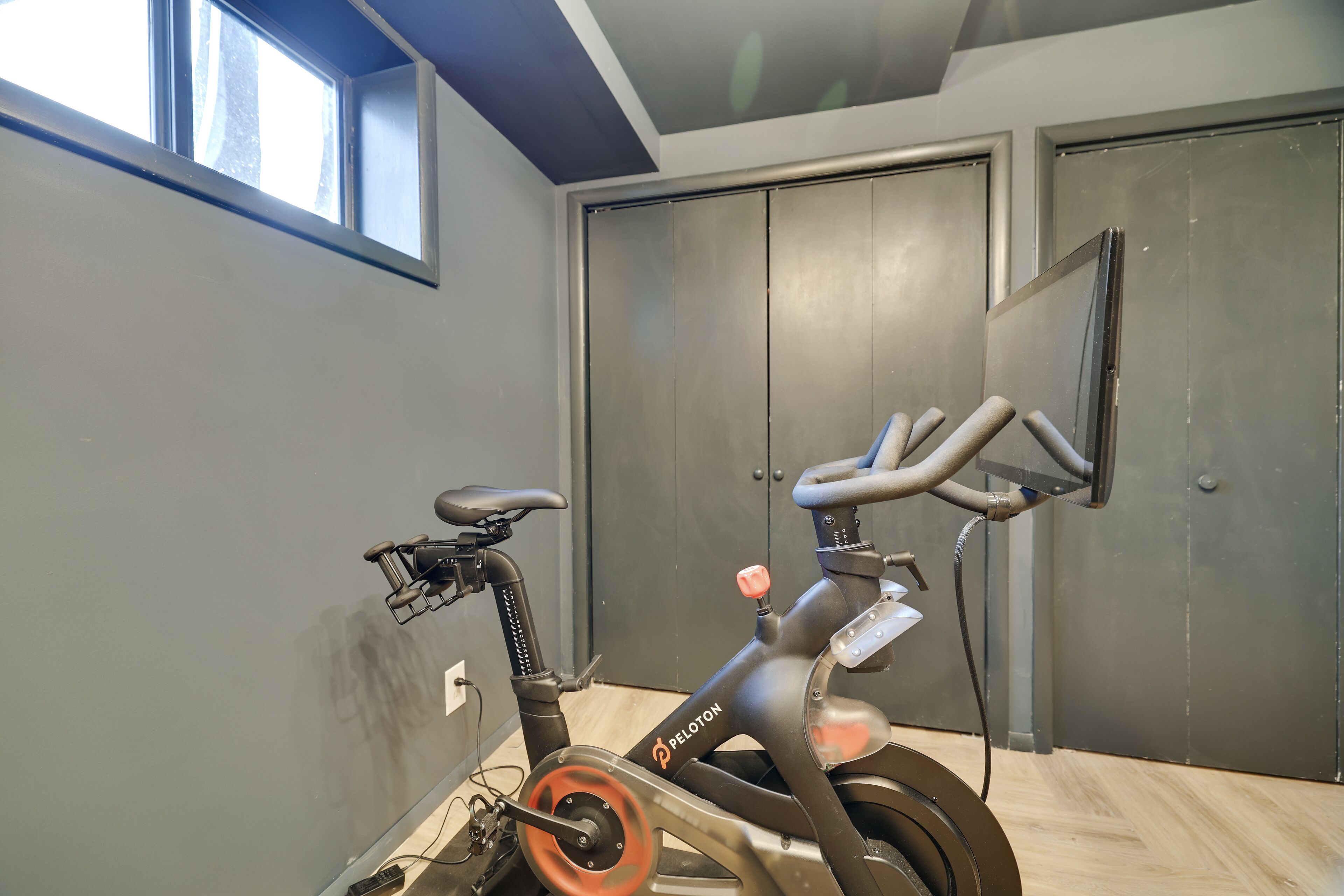 Una bicicleta estática en una habitación con una ventana, una puerta y un espejo fijado a la pared.