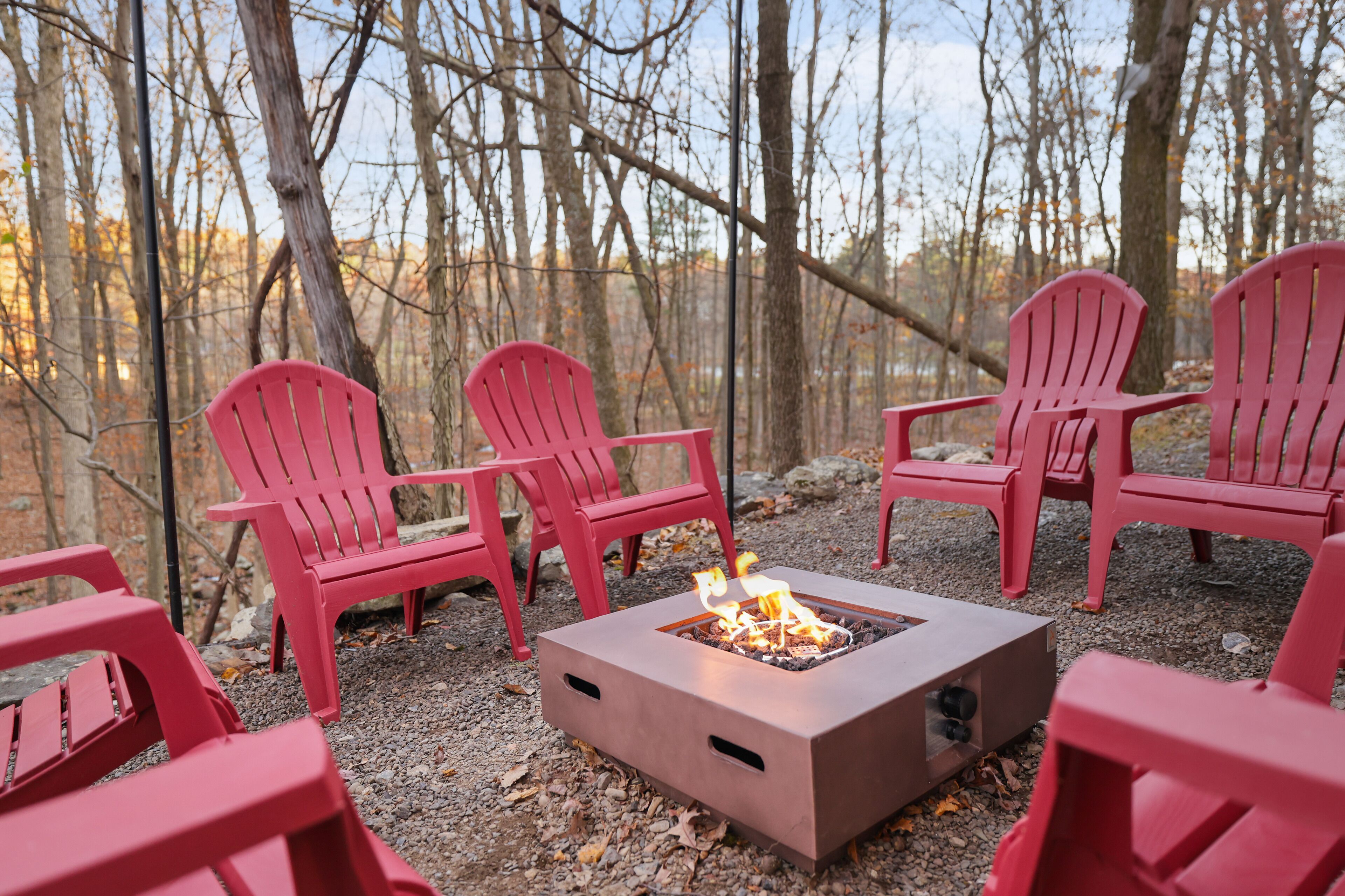 A fire pit surrounded by red Adirondack chairs in a wooded area.
