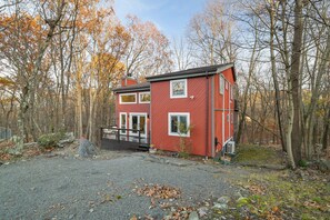 A red two-story house with a front porch, surrounded by trees and a gravel driveway.