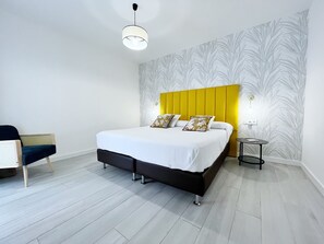 Une chambre à coucher moderne avec un lit, une chaise, une table de chevet et un mur orné d’un motif de feuilles.
