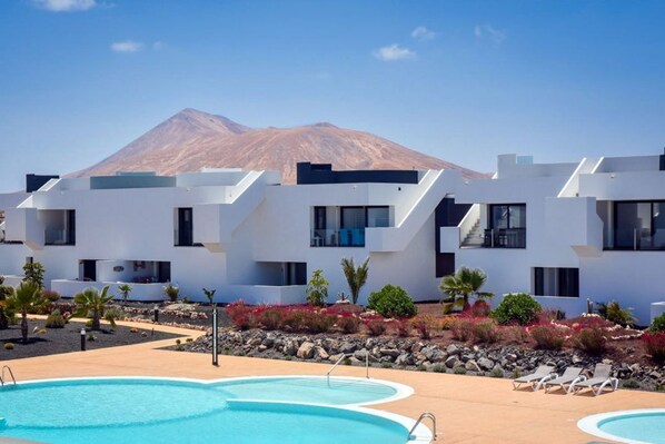 Un hôtel moderne doté d’une piscine, de bâtiments blancs et offrant une vue sur une montagne en arrière-plan.