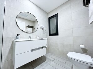 Une salle de bain moderne avec un meuble-lavabo blanc, un miroir rond, un sèche-cheveux et des toilettes.