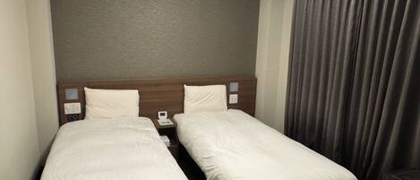A hotel room with two single beds, a wooden headboard, a nightstand with a phone, and a large window with curtains.