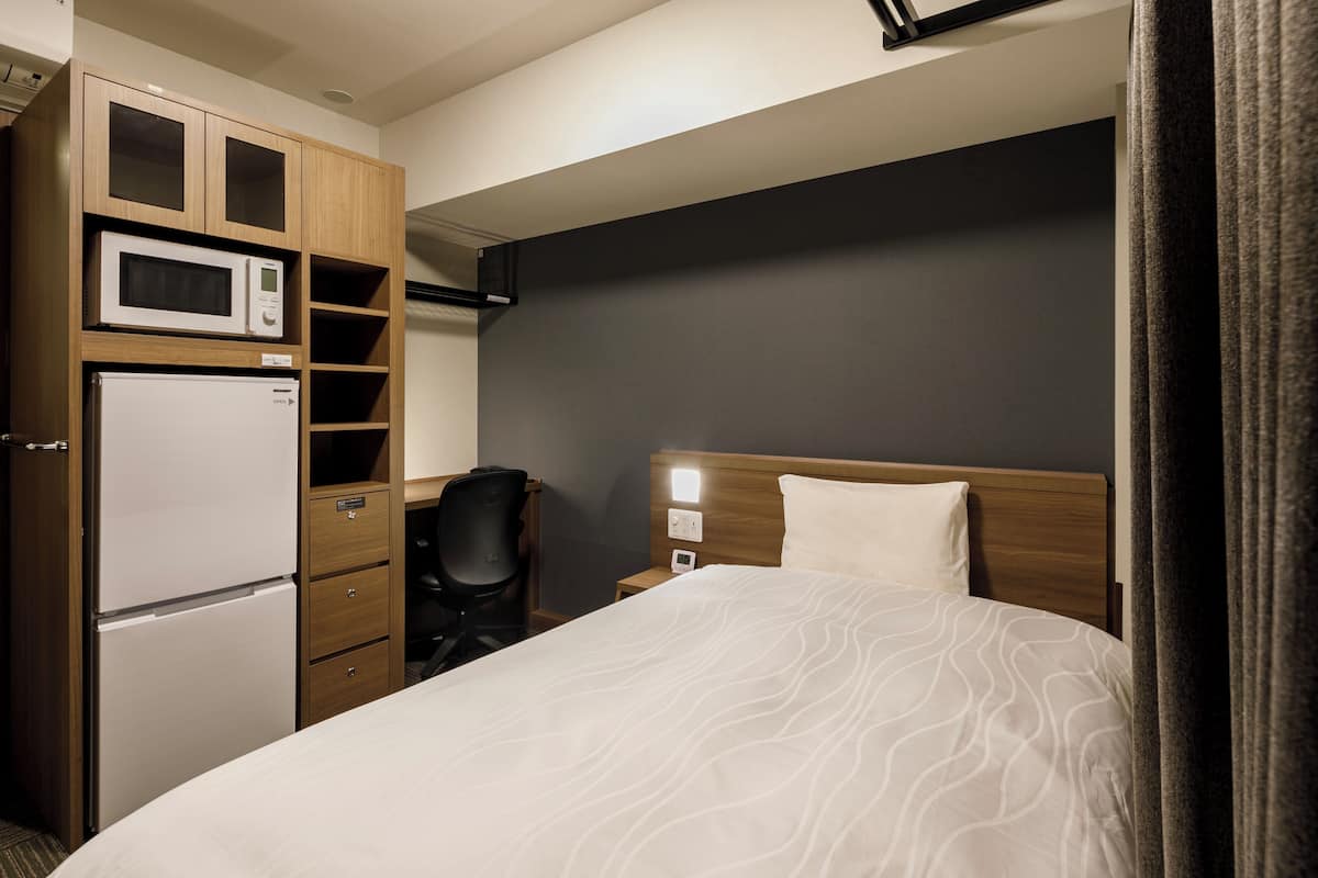 A hotel room with a bed, a microwave, a refrigerator, a desk, and a chair.