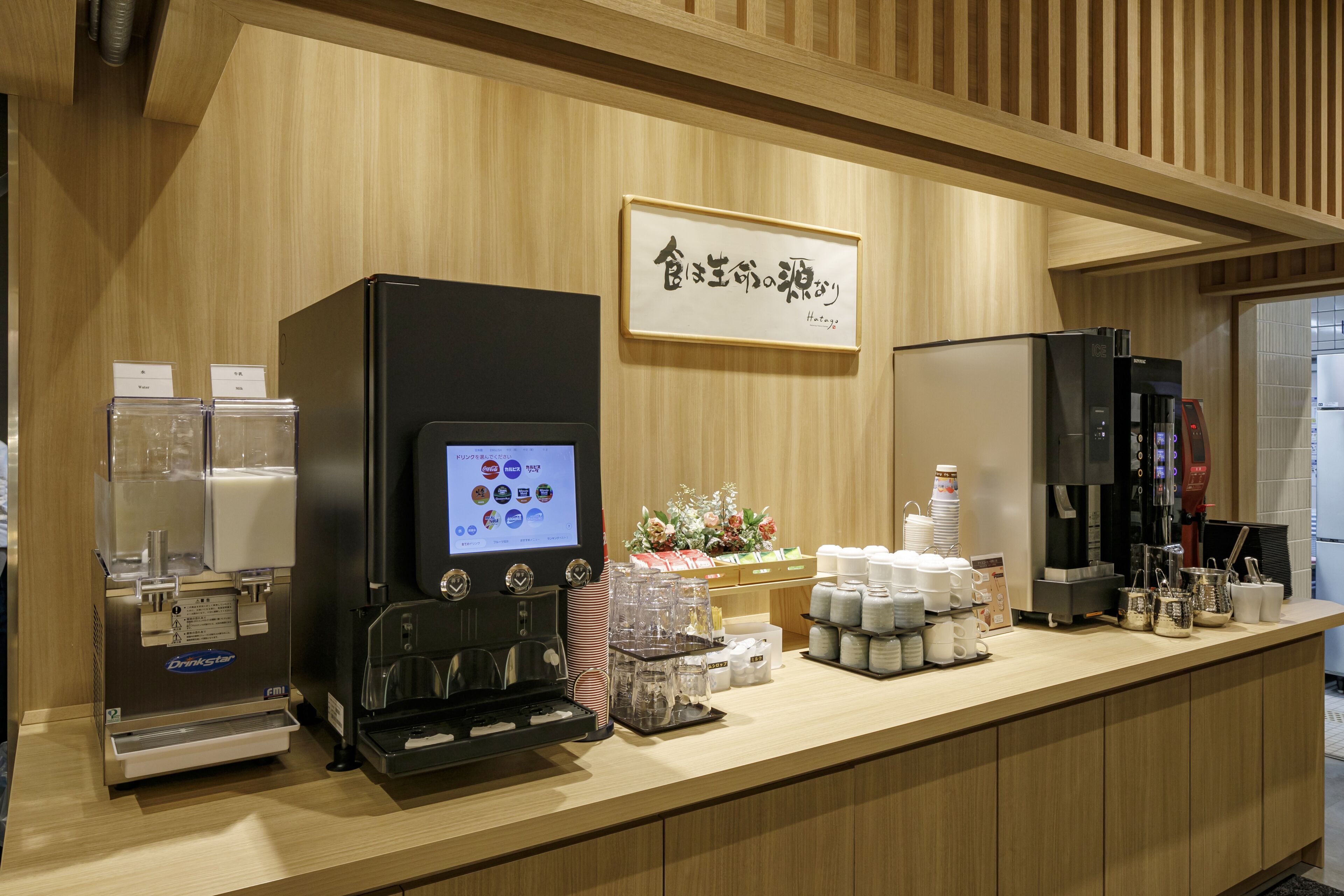 A coffee station with a digital menu, a coffee machine, and a refrigerator.
