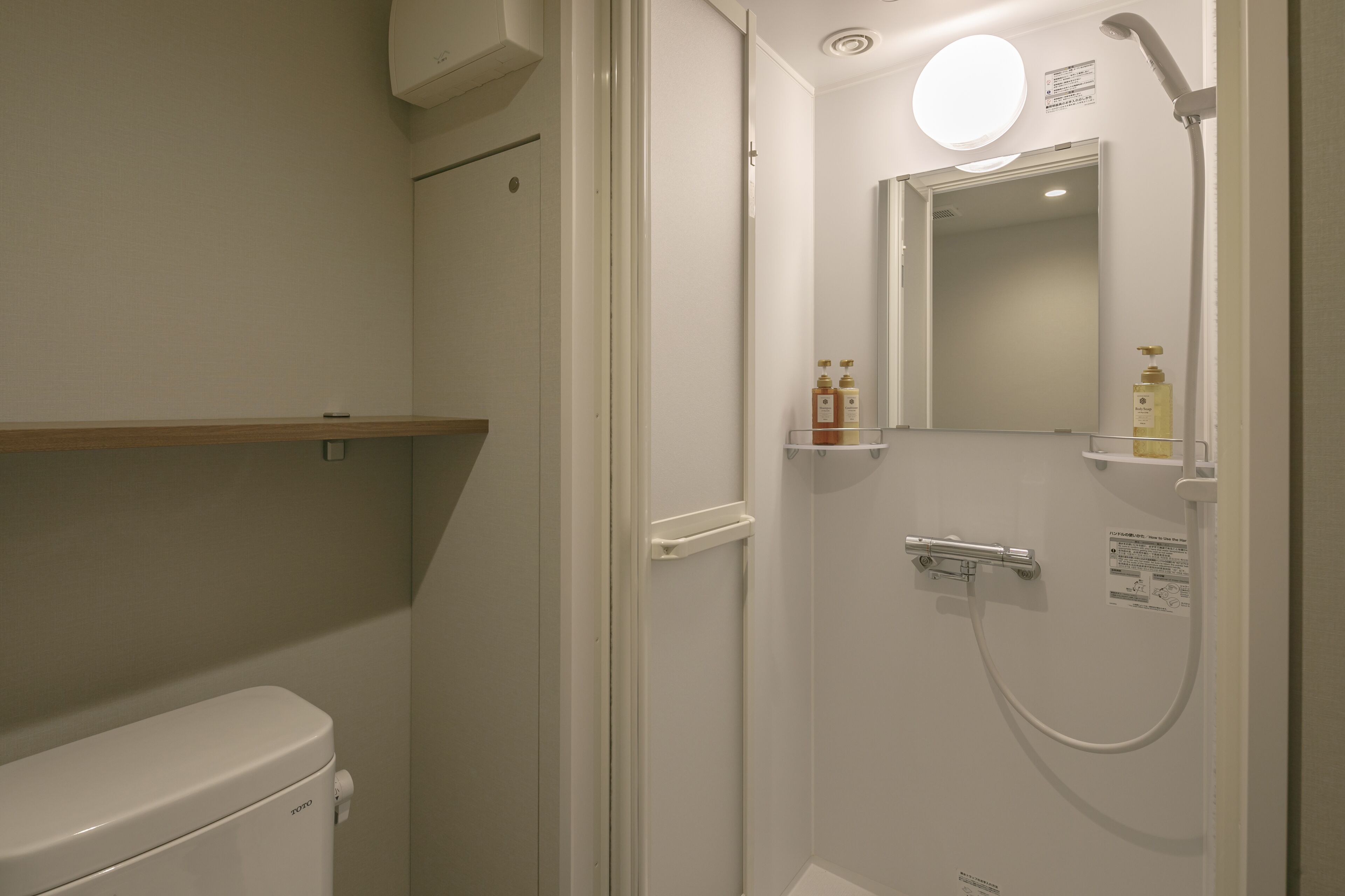 A modern bathroom with a toilet, a shower with a handheld showerhead, and a mirror with a shelf holding toiletries.