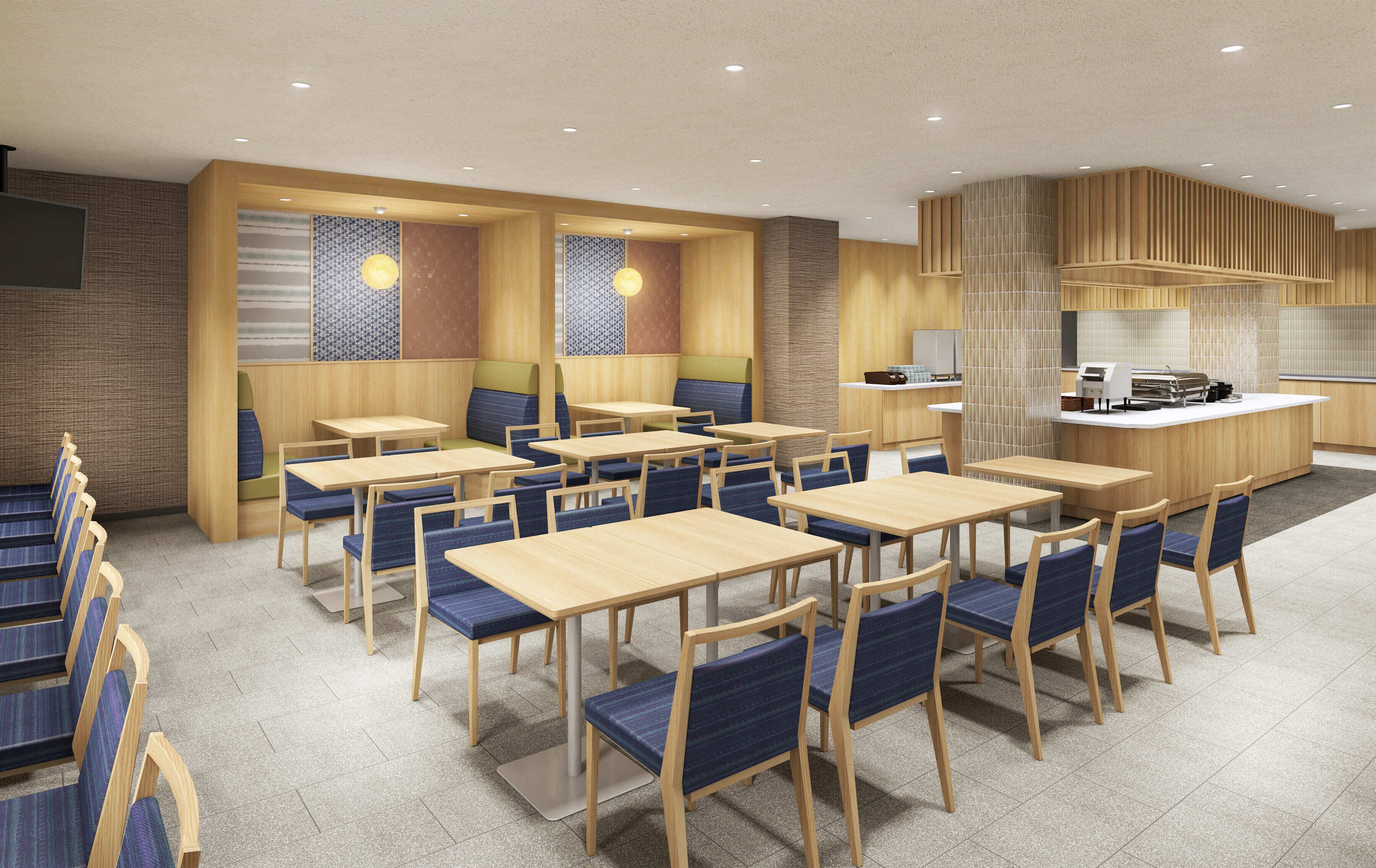A modern restaurant with wooden tables and blue cushioned chairs, a central bar area, and a kitchen visible in the background.