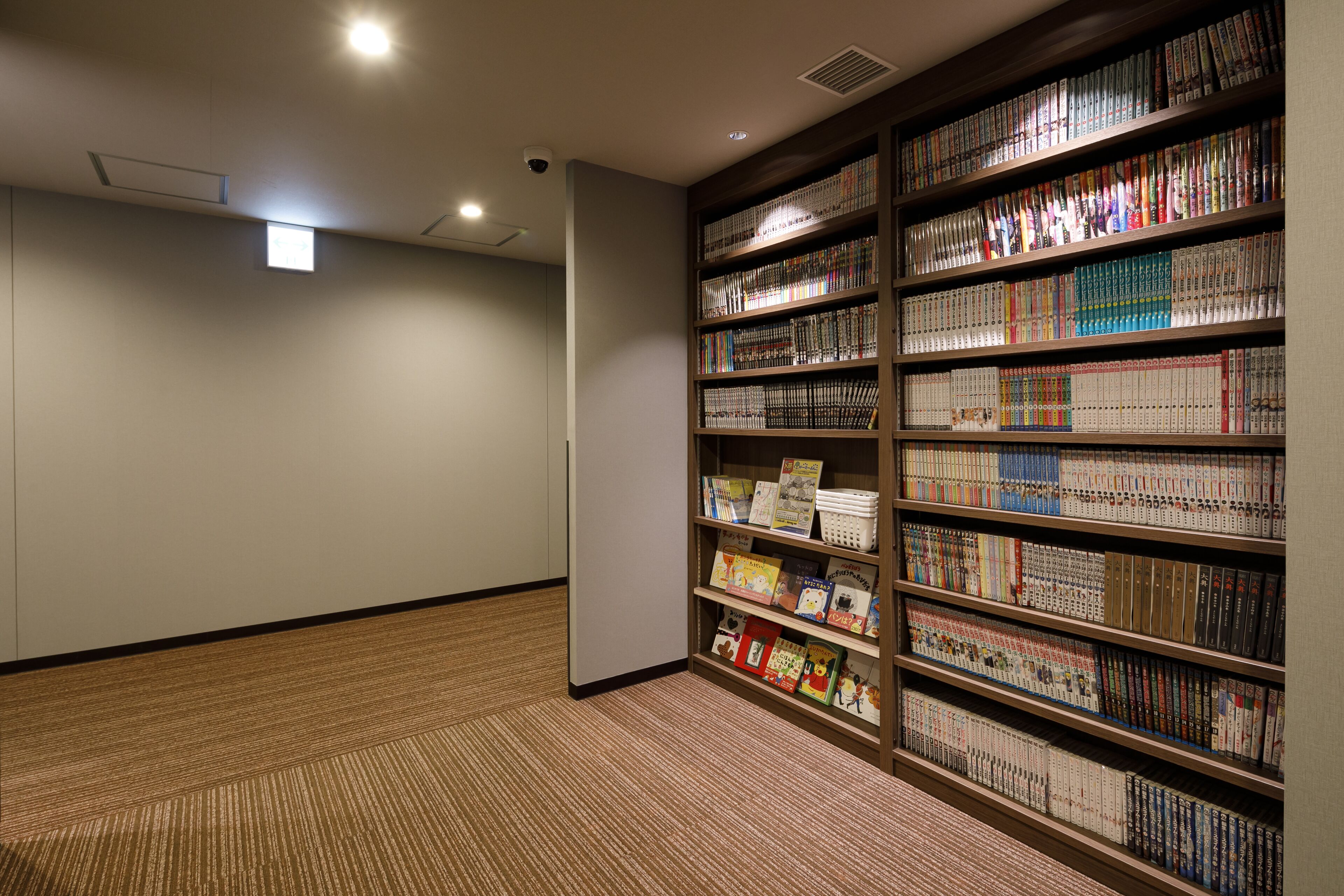 Una biblioteca con estanterías llenas de libros, suelo alfombrado e iluminación en el techo.