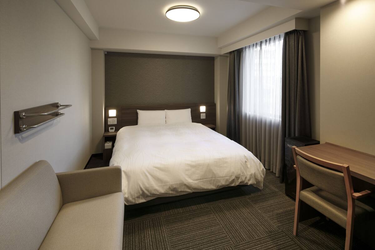 A hotel room with a bed, a desk, a chair, and a nightstand.