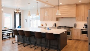 Une cuisine moderne dotée d’un grand îlot central, de tabourets de bar, d’appareils électroménagers en acier inoxydable et de luminaires suspendus.