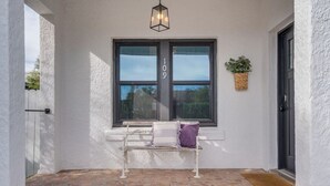 Eine terrasse mit steinbelag, eine weiße Bank, eine schwarze Tür und eine hängende Leuchte.