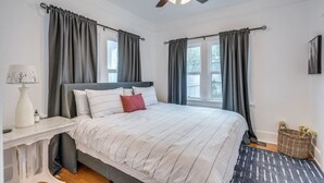 Ein Schlafzimmer mit Bett, Nachttisch, Lampe, Deckenventilator und einem Fenster mit Vorhängen.