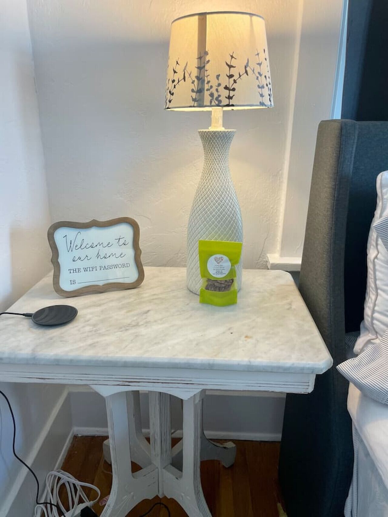 A small white table with a lamp, a sign reading "Welcome to our home," and a small green bag.