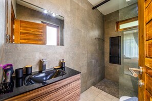 A modern bathroom with a wooden vanity, a large mirror, and a glass shower enclosure. - Secluded Oasis for Family - BM5 (Hua Hin)