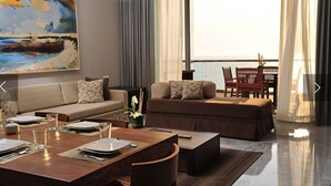 A modern living room with a sofa, ottoman, dining table set for four, and a large painting of a beach scene. - PGA Tour - Luxury Suite steps from the course! (Nuevo Vallarta)
