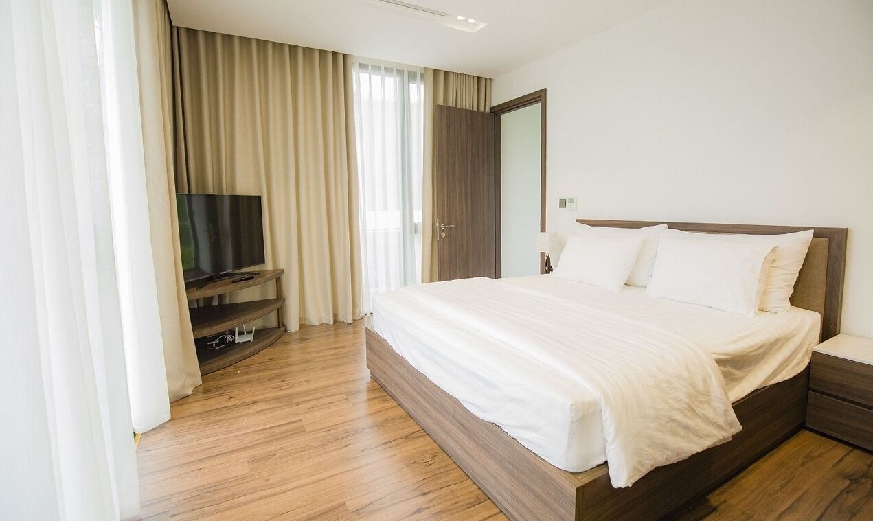 A modern hotel room with a large bed, a flat-screen TV, and a wooden floor.