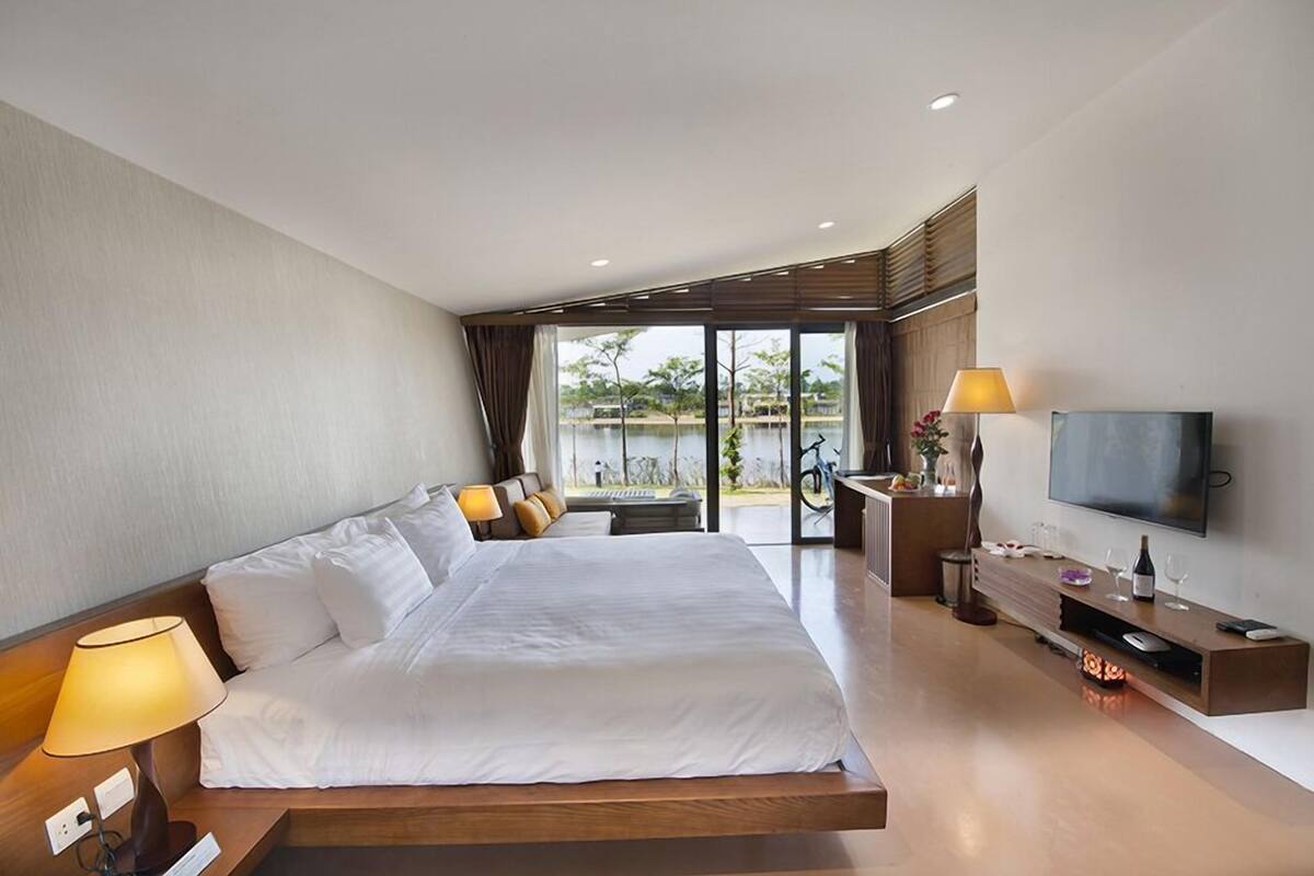 Une chambre d’hôtel moderne dotée d’un grand lit, d’une télévision, d’un bureau avec une lampe et offrant une vue sur l’extérieur.
