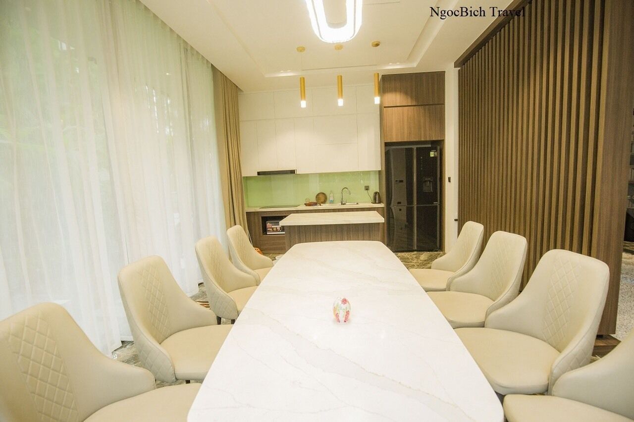 A conference room with a long table and eight chairs, a kitchen area in the background, and a wooden panel wall.
