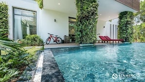 A modern pool area with a clear pool, red lounge chairs, and a bicycle. - Flamingo Dai Lai Resort Vila Tu Nhan BBQ (Vinh Phuc)
