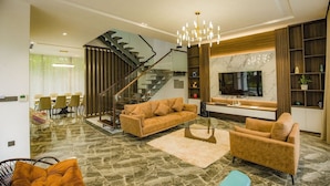 A modern living room with a sofa, coffee table, and a TV. There is a staircase leading to another level. - Flamingo Dai Lai Resort Vila Tu Nhan BBQ (Vinh Phuc)