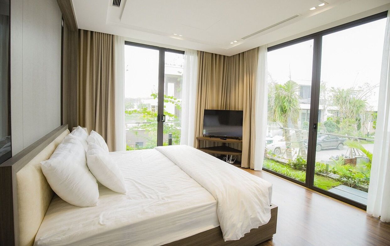 Habitación de hotel moderna con una cama grande, un televisor de pantalla plana y amplios ventanales que ofrecen vistas al exterior.