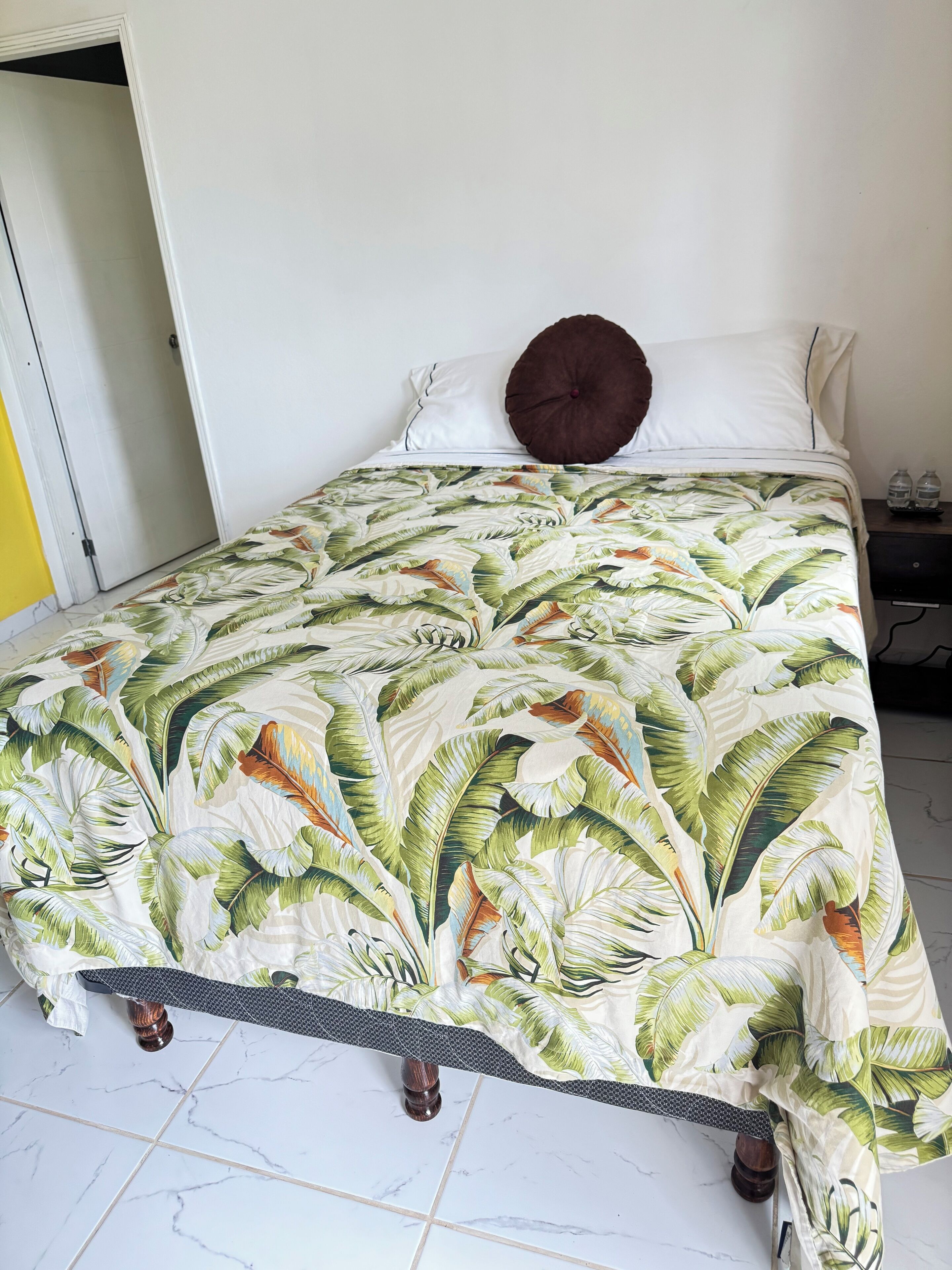 A bed with a tropical leaf-patterned bedspread, white pillows, and a brown accent pillow.