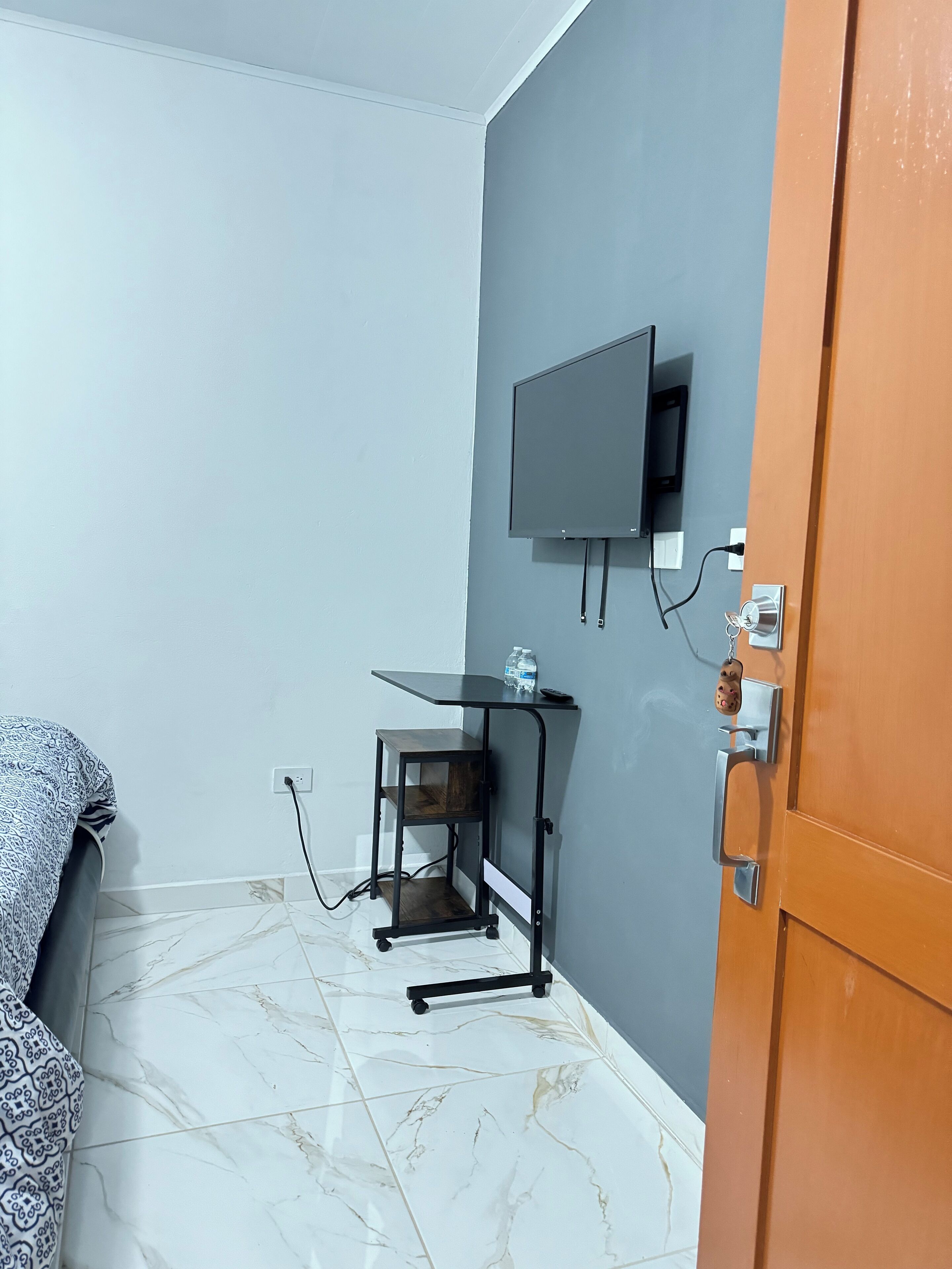 Een kleine kamer met een bed, een bureau met een televisie en een deur.