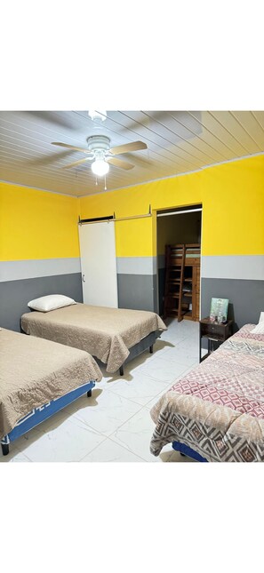 Ein Zimmer mit zwei Betten, einem Deckenventilator, einer Tür und einem kleinen Tisch mit Stuhl.