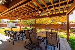 An outdoor patio with a wooden ceiling and a ceiling fan, surrounded by chairs and a table. - Northern New Mexico Home Perfectly Located!   (Aztec)