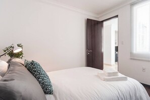 Una camera da letto con un letto, cuscini, una lampada sul comodino e una porta che dà su un'altra stanza.